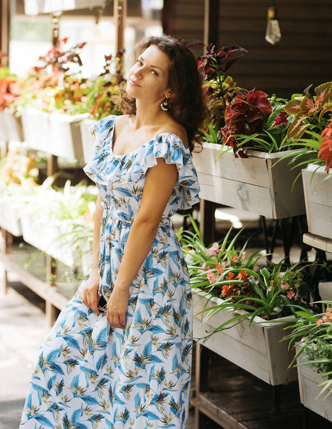 Bright girl with brunette curly long hair and red earrings in trendy green sundress laughing and posing on floral background. femine - Φωτογραφία, εικόνα