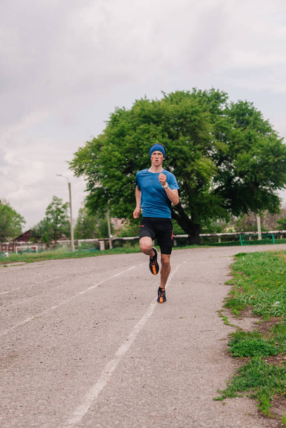 A young athlete in a blue T-shirt runs around the stadium - Fotoğraf, Görsel