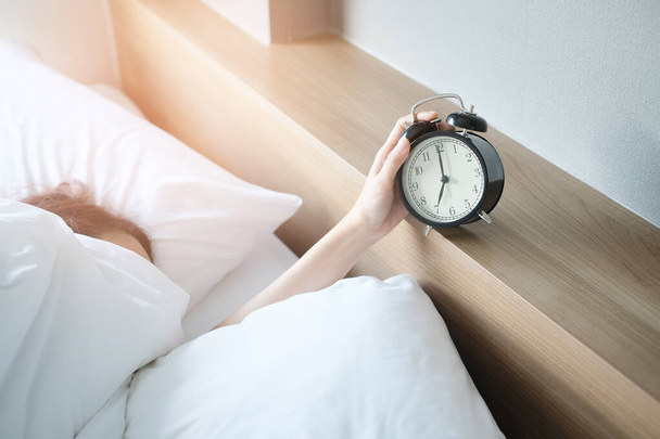 Женщина спит на кровати выключает будильник просыпается утром, выборочный фокус. - Фото, изображение