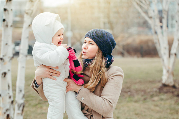 Šťastně se usmívající mladá běloška matka drží dceru venku na jaře. Rodina dva lidé spolu venku na venkově nebo ve městě. Autentický životní styl s kojeneckými dětmi.  - Fotografie, Obrázek