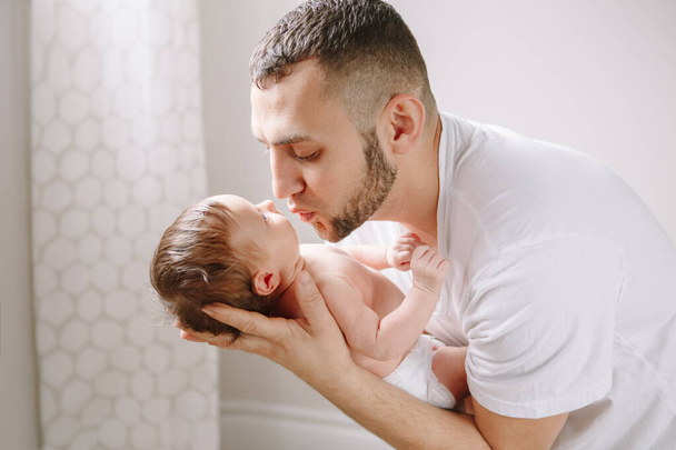 Happy young Caucasian father kissing newborn baby. Dad man parent holding rocking child daughter son on his hands. Authentic lifestyle candid family moment.  Fathers Day holiday. - Photo, Image