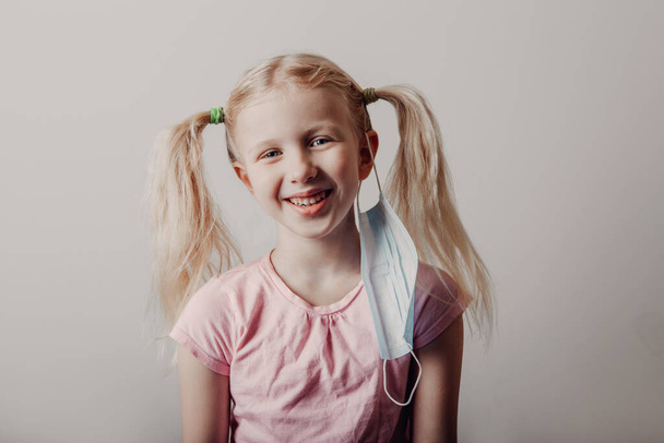 Portrait of Caucasian blonde girl taking off sanitary face mask. Preschool child with protective mask on her ear. End finish of covid-19 quarantine and self isolation concept. - Valokuva, kuva