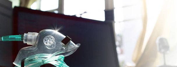 Ιατρική συσκευή Ατομική φορητή μάσκα οξυγόνου για την τοποθέτηση αέριου αερίου για ασθενείς με αναπνευστικές διαταραχές, θολό υπόβαθρο της επιχειρησιακής οθόνης, παράθυρα, κουρτίνα, μικρόφωνο και φως του ήλιου - Φωτογραφία, εικόνα