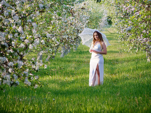 girl with a white umbrella in blooming apple trees in the garden 2020 - Foto, Imagen