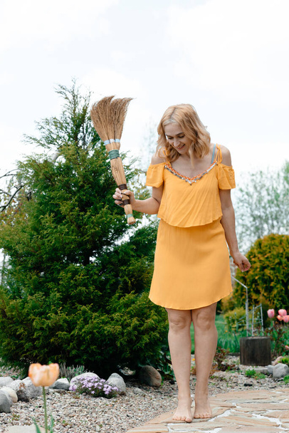 cute woman in yellow dress posing with broom outdoors  - Foto, afbeelding
