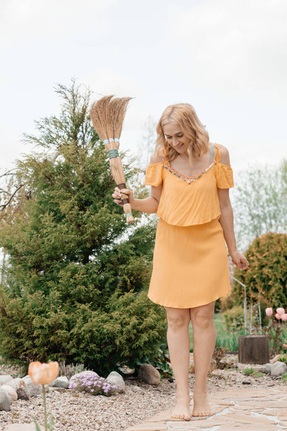 cute woman in yellow dress posing with broom outdoors  - Fotó, kép