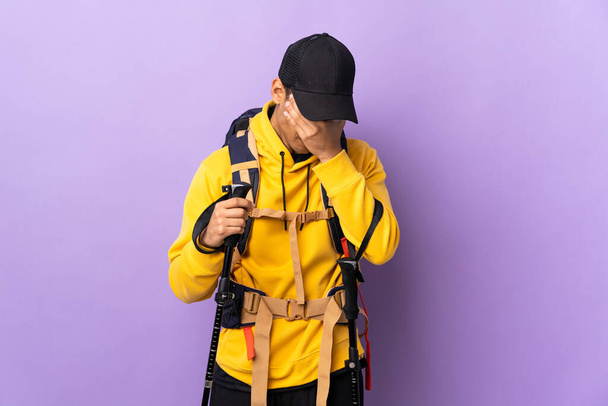 Hombre afroamericano con mochila y bastones de trekking sobre fondo aislado con expresión cansada y enferma
 - Foto, imagen