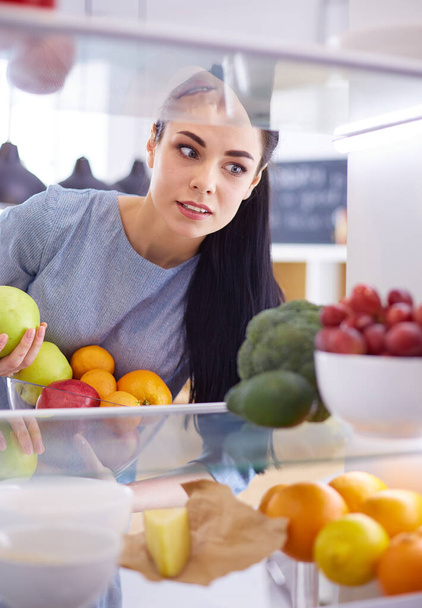 Mulher sorridente tirando uma fruta fresca da geladeira, conceito de comida saudável - Foto, Imagem