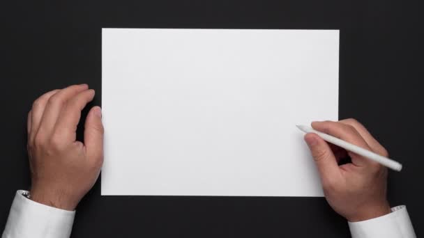 felső nézet egy üres papírlap és egy üzletember kezét egy fekete asztal, fehér ing és karóra - Felvétel, videó