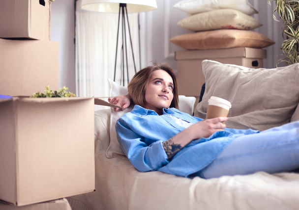 Happy young woman lying on sofa at new home , drinking coffee or tea - Photo, image