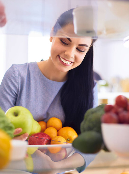 Smiling woman taking a fresh fruit out of the fridge, healthy food concept - Foto, Bild