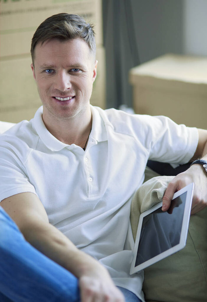 Portrait of happy young man moving in new home. Man holding digital tablet in his arms - Фото, зображення