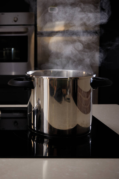Pot avec de l'eau bouillante dans la cuisine. La casserole est située sur la plaque à induction avec cuisine inférieure
. - Photo, image