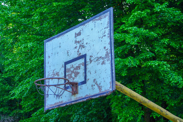  Oude basketbalring in het park met groene bomen als achtergrond. - Foto, afbeelding