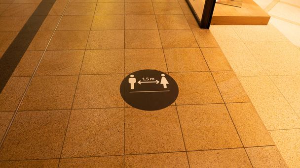 Een waarschuwingsbord voor sociale afstand op de grond in een winkelcentrum. Het teken werd geplaatst vanwege het coronavirus. - Foto, afbeelding