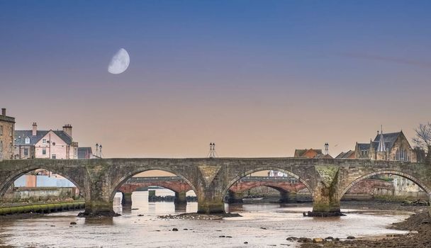 El Auld Brigg o puente que conduce al centro de la ciudad de Ayr que está en el corazón del país de Burns wityh media luna temprano en la mañana
. - Foto, imagen