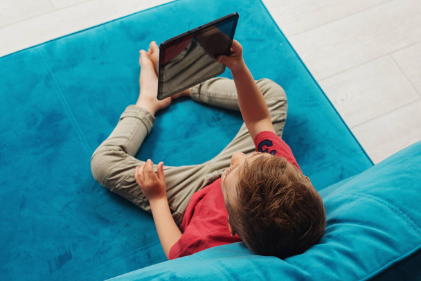 Preschooler watches tablet at home on the couch - Fotó, kép