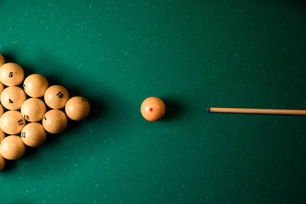 Billiard balls and cue on the billiard table, top view, flat lay.Top view billiard cue and pyramid of yellow pool balls on green billiard table. - Fotó, kép