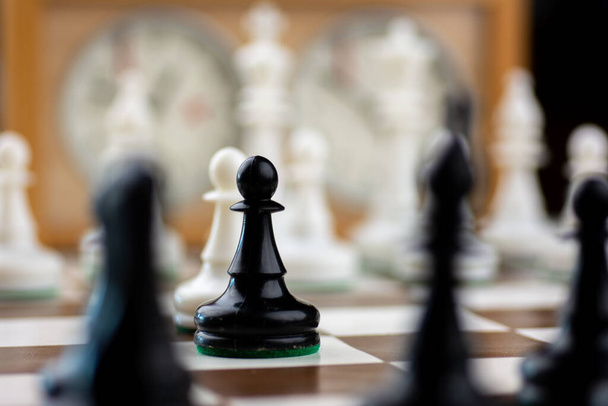 Черно-белые пластиковые шахматные фигуры на коричнево-белой шахматной доске с шахматными часами
 - Фото, изображение