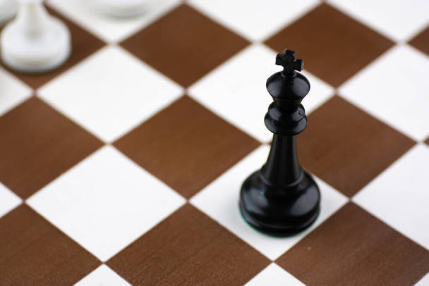 Schwarz-weiße Plastikschachfiguren auf einem braun-weißen Schachbrett mit Schachuhr - Foto, Bild