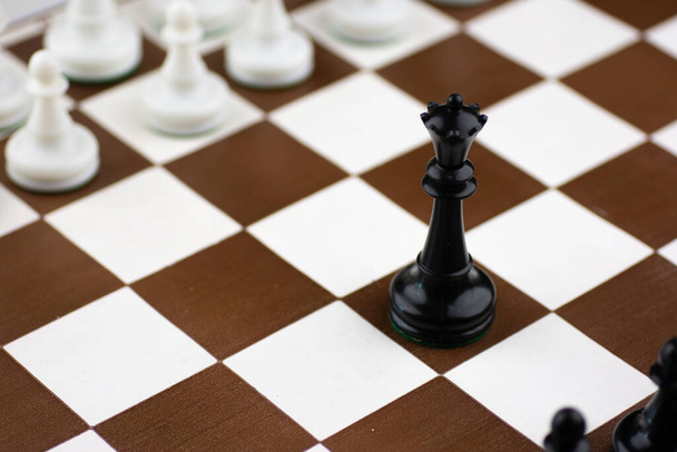 Черно-белые пластиковые шахматные фигуры на коричнево-белой шахматной доске с шахматными часами
 - Фото, изображение