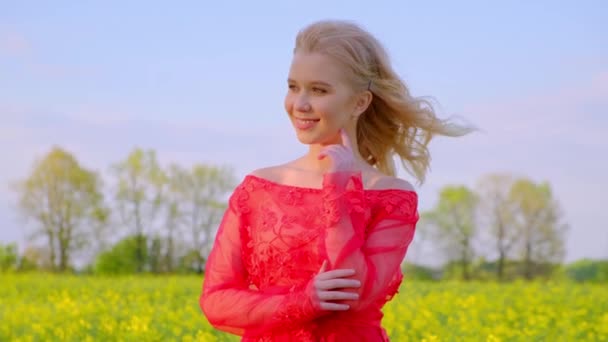 Πορτρέτο του Smiling κορίτσι με μακριά ξανθά μαλλιά στο καπέλο περπάτημα στο πεδίο. Ηλιόλουστη μέρα. Αργή κίνηση. Teen κορίτσι φορώντας σε όμορφο κόκκινο φόρεμα που θέτουν σε Yelllow φόντο τομέα - Πλάνα, βίντεο