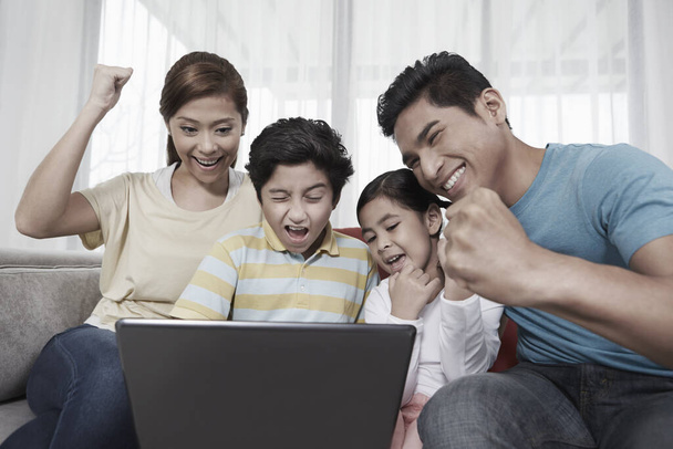 Family of four sitting and using laptop together - Photo, image