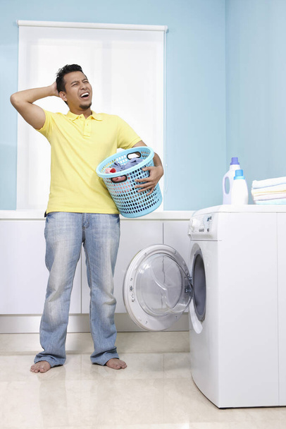 Man scratching head while holding laundry basket - Фото, зображення