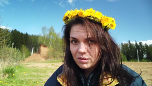 Mooi glimlachend brunette meisje met een krans van paardenbloemen op haar hoofd op - Video