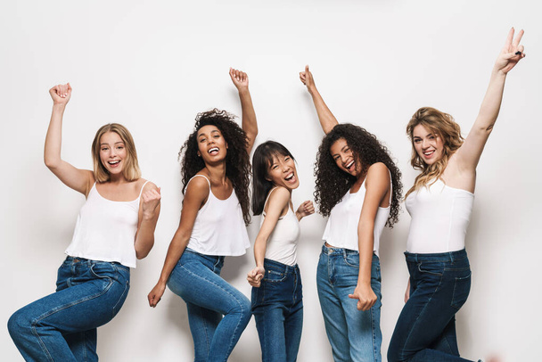 Image of excited multinational women in blue jeans smiling and gesturing peace sign isolated over white background - Foto, Imagem