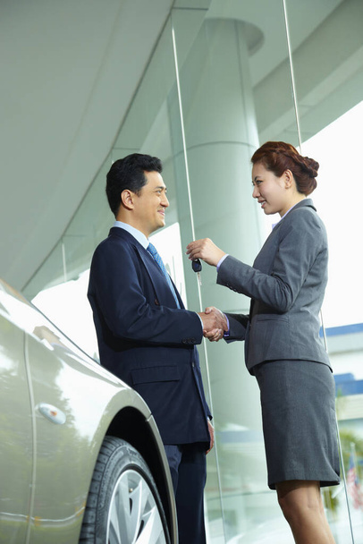 Sales representative handing over keys to customer in car showroom - Foto, immagini