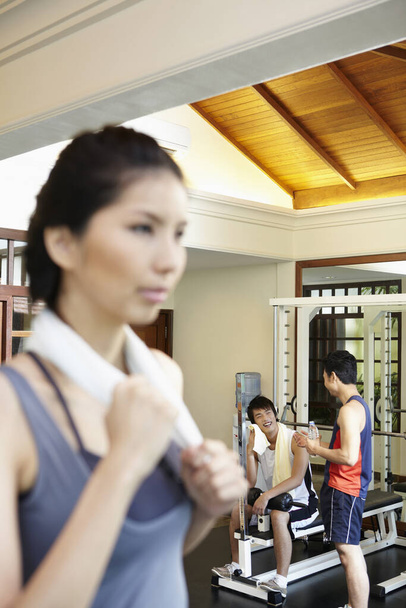 Woman exercising in gym, men talking in the background - Photo, Image