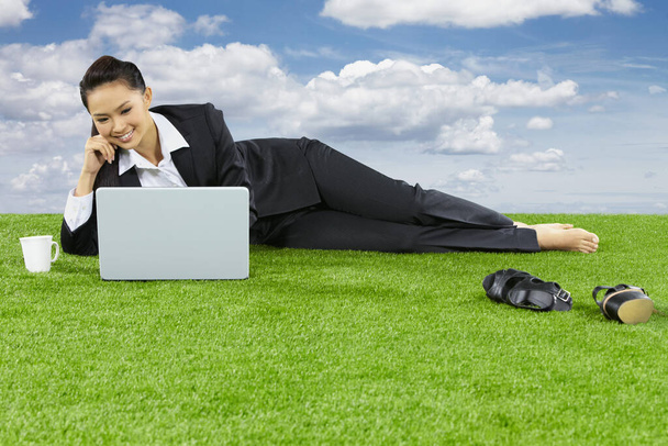 A relaxed young Asian businesswoman lying on grass using her laptop - Foto, imagen