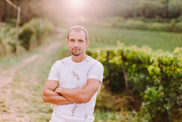 портрет мужчины с закрытыми руками в сельской местности. Красивый мужчина в сельских виноградниках смотрит в камеру. Владелец фермы. Италия - Фото, изображение