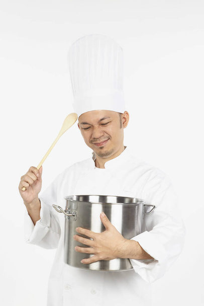 Asian chef holding a stew pot and a wooden spoon, looking stressed - Foto, Imagen