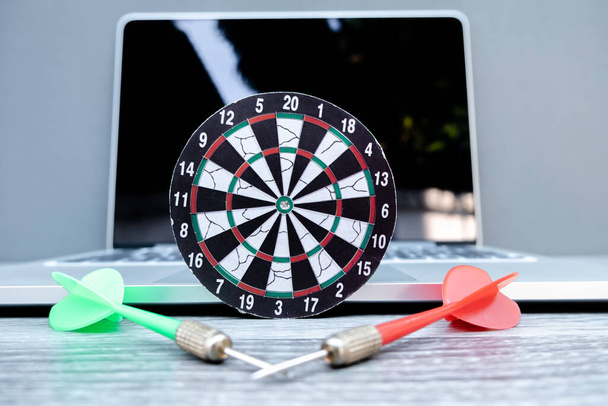 Het kleine dartbord en de pijl gelegen met laptop vertegenwoordigen succesvolle zakelijke doelen concept. - Foto, afbeelding