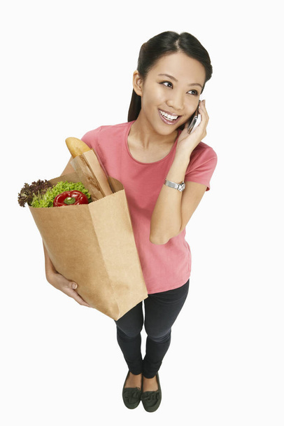 Woman talking on the phone while carrying groceries - Фото, изображение