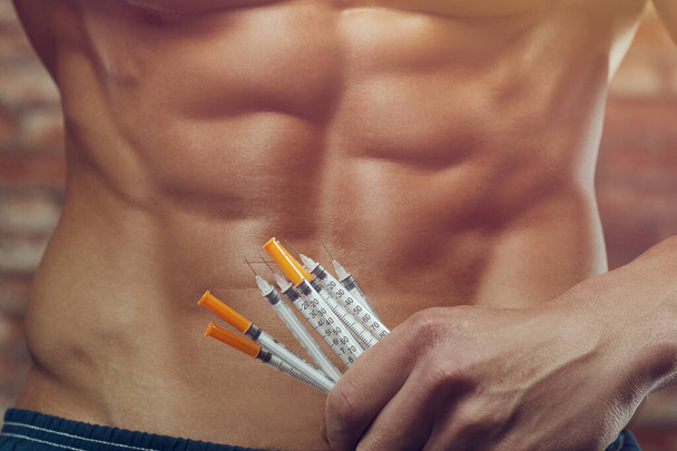 Bodybuilder doing steroid syringe injection in gym. Strong athletic rough muscular man pumping up abs muscles workout fitness and bodybuilding healthy concept design. abdominal exercises naked torso - Photo, image