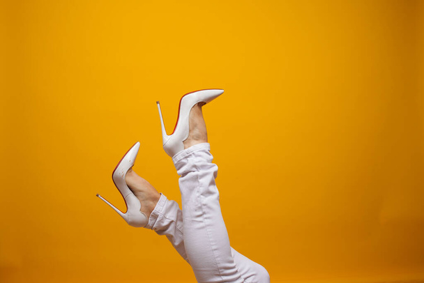 Female feet in beautiful white stiletto shoes, yellow background copy space. - Zdjęcie, obraz