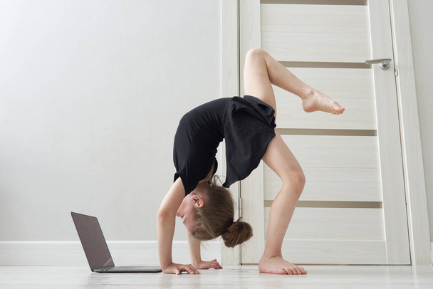 Little girl doing gymnastics exercises at home using online learning with laptop computer, internet education concept - Foto, afbeelding