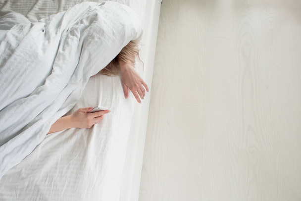 Morning, the woman under the blanket, turns off the alarm clock - Foto, afbeelding