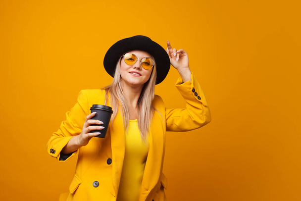 Take-away coffee. Stylish trendy young woman in bright clothes on a yellow background. - Fotografie, Obrázek