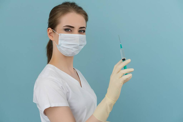 woman doctor in mask and gloves holds a syringe in hand on a blue background - Photo, image