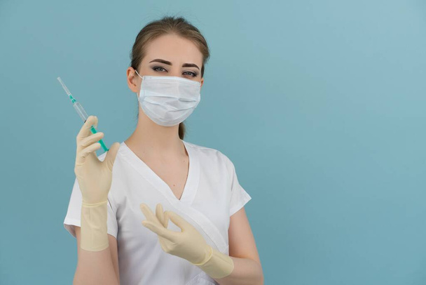 woman doctor in mask and gloves holds a syringe in hand on a blue background - Foto, imagen