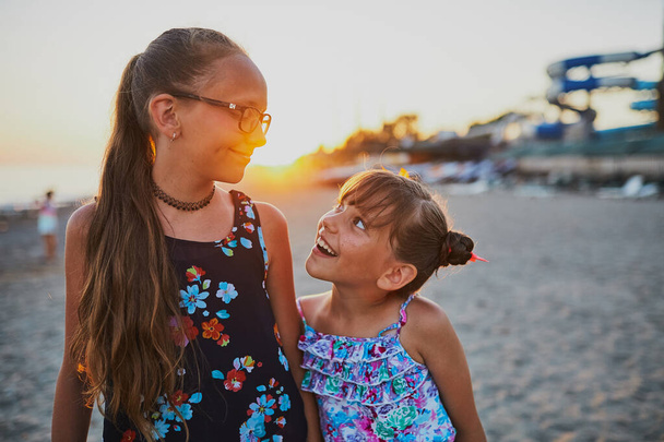 Dwie siostry bawią się na plaży o zachodzie słońca. Na tle parku wodnego. - Zdjęcie, obraz