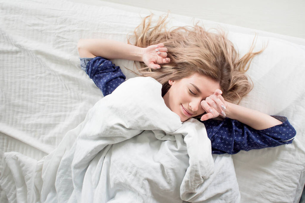 Cute blonde in her bed in blue pajamas, under a blanket - Foto, Imagem