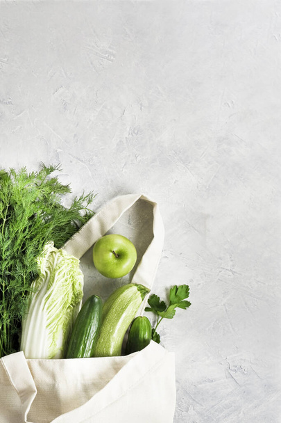 Various fresh vegetables and fruits, greenery in a reusable shopping cotton bag on a concrete gray tabletop,food blog. Zero waste shopping concept.Vertical Top view with copy space. - Фото, зображення
