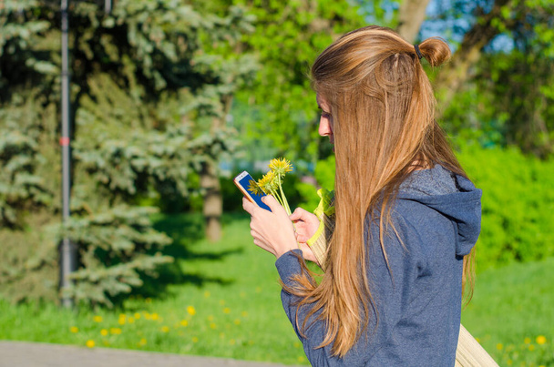 young woman in medical mask texting message and tapping on mobile phone in park outdoors. Virus and allergic concept - Foto, immagini