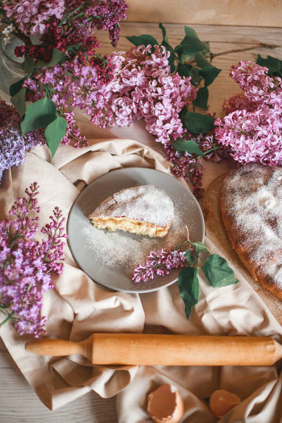 Homemade Apple pie on a wooden table next to a bowl of lilacs. Gentle toning. Selective focus. - Foto, Imagen