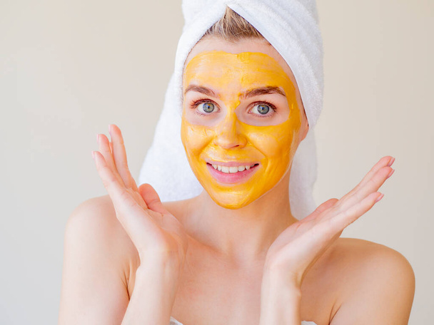 Pleťová krása a SPA procedury. Portrét mladé ženy s ručníkem na hlavě při aplikaci přírodní pleťové masky doma - Fotografie, Obrázek